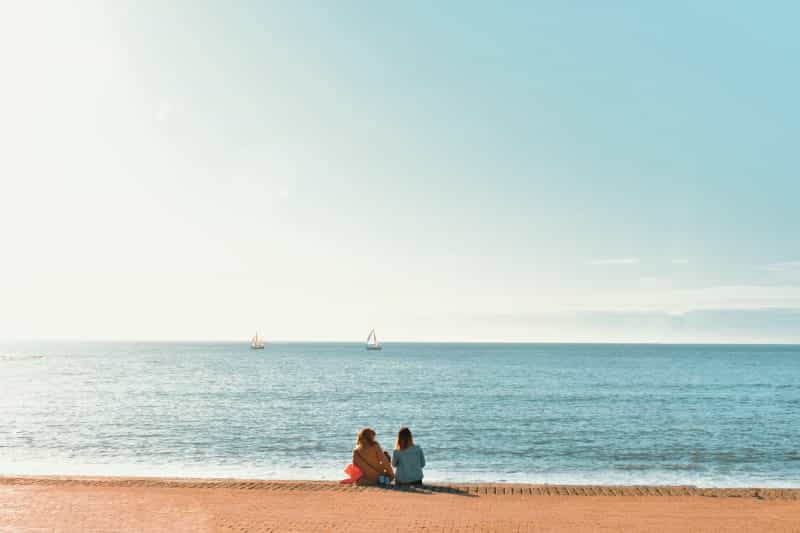 Two people sit and look out at the sea near the student town of Aberystwyth (Jordan Ling / Unsplash)
