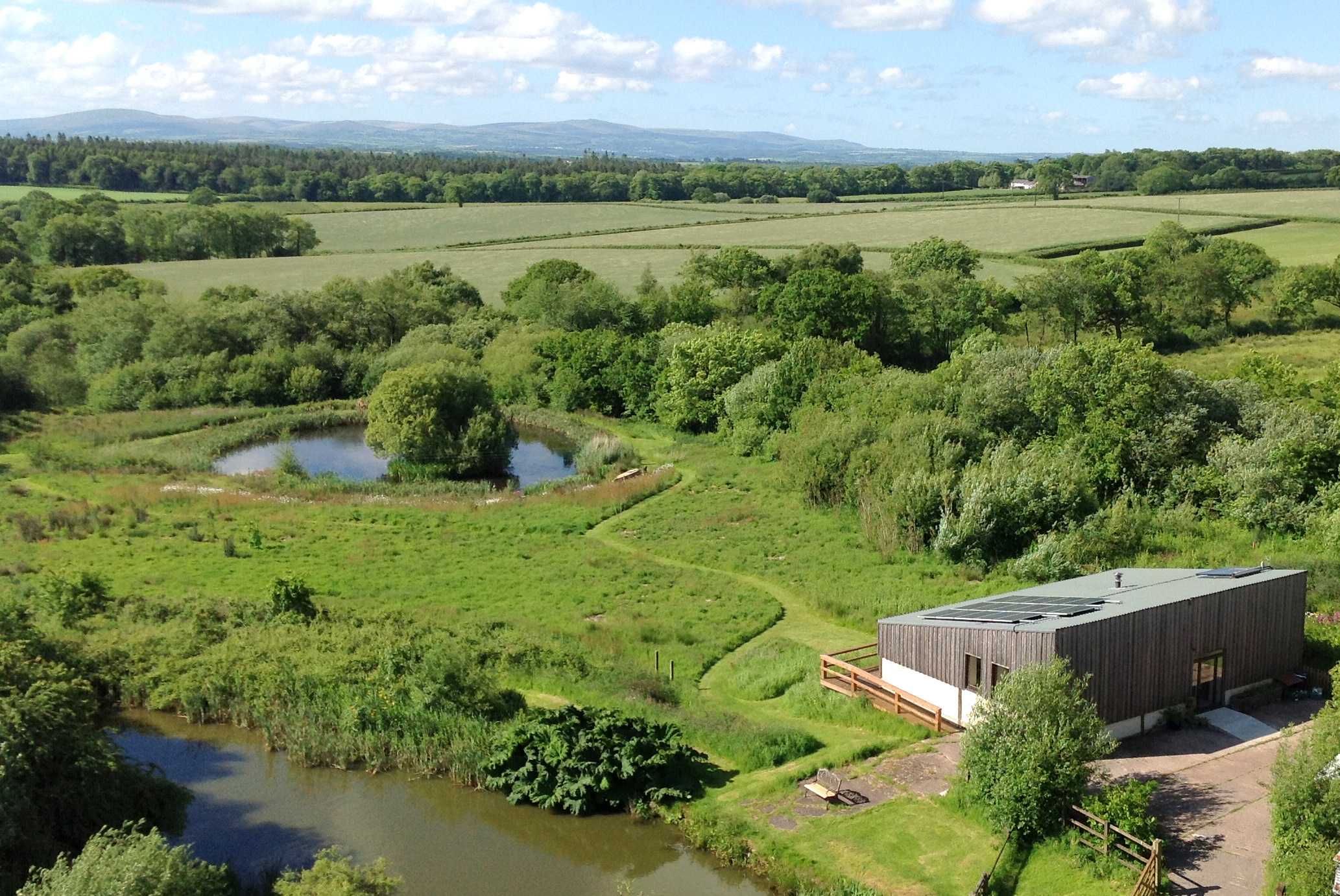 An aerial view shows a wheelchair accessible cabin looking over a meadow, with a step free path to a fishing pond
