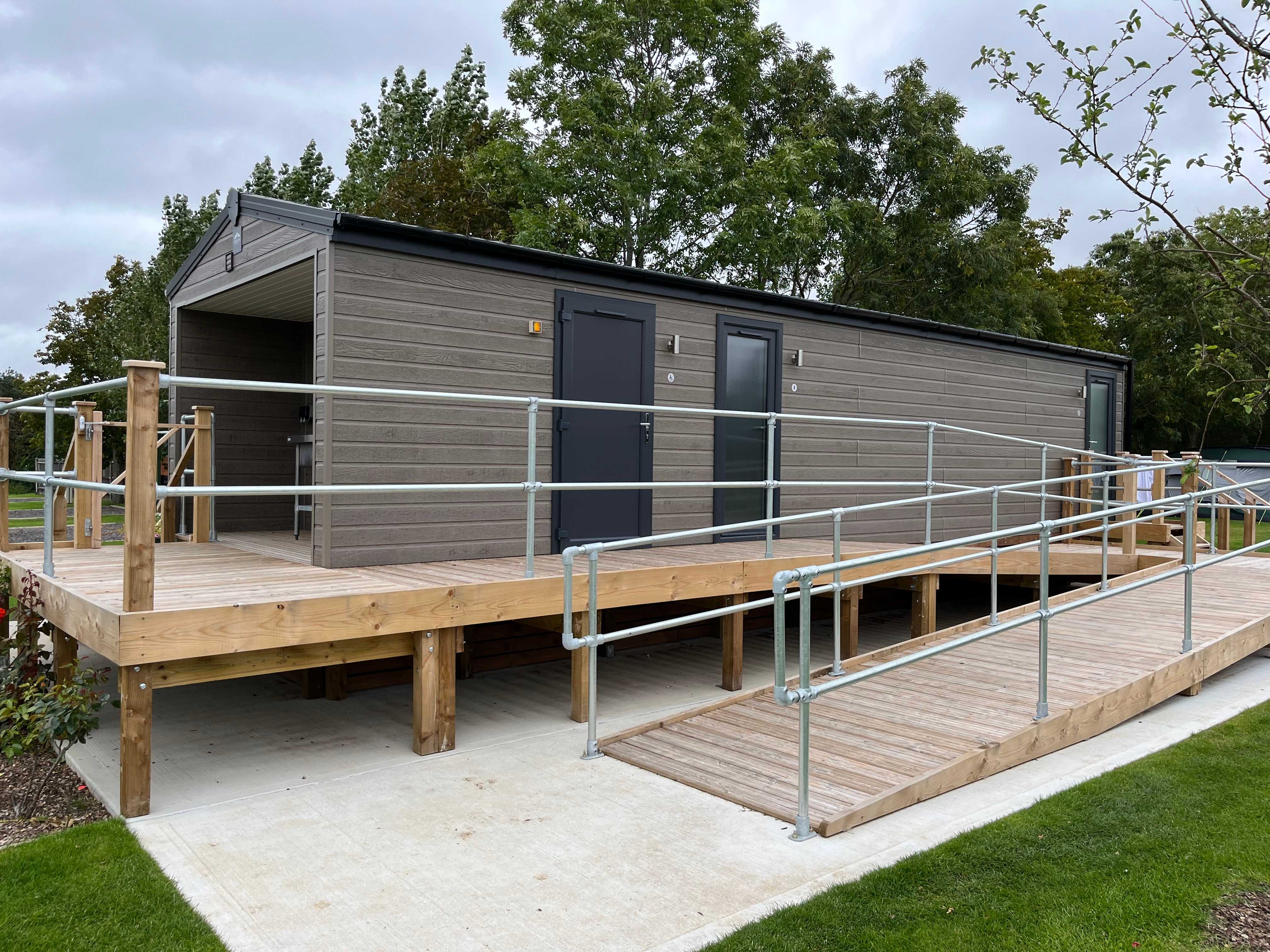 The photo shows a cabin with bathroom and washing facilities, with a wheelchair access ramp leading to the entrance