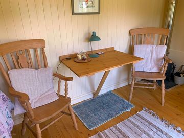 Shepherd's hut with a fold-down table, two carver chairs and hobbit woodburner