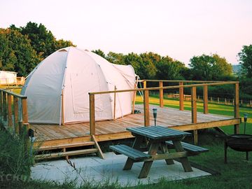 Bell tent on decking, with picnic table and firepit