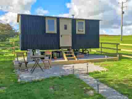 Shepherd's hut with a small gravelled patio area, bistro table, chairs and picnic table