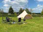 Six-metre bell tent with picnic bench, barbecue and camp chairs around the firepit