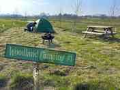 Grass pitch with picnic bench and fire pit area with pond and countryside views.