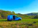 Blue van parked on grass with hills and woodland behind