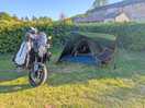 Bike and a tent in with the toilet and shower block behind the hedge at the rear.