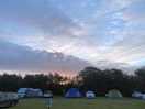 Early morning sunrise, puffy clouds and tents in the field