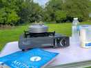 Camping table with small gas stove, kettle and book and views across a quiet camp site