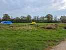 A photograph of a large, grassy field backed by trees. there is a blue tent and a yellow van.