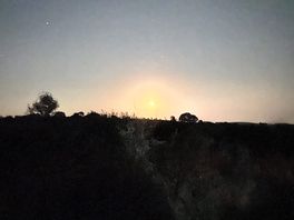 An orange moon rises over the hills at night with stars in the sky above.