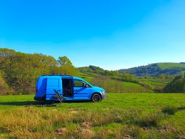 Blue van parked on grass with hills and woodland behind