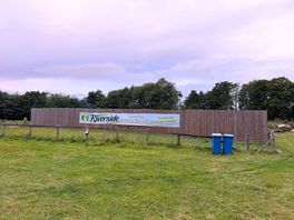 Riverside campsite well signpost with bins for rubbish disposal.