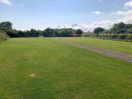 View of main field down towards children’s play area, small shop and shaded seating area.