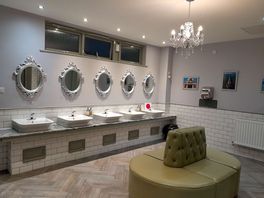 Ladies toilets with sinks & mirrors and large sofa.