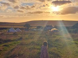 Sunset at mwnt campsite, the sun shining through clouds. a small child on the foreground is watching