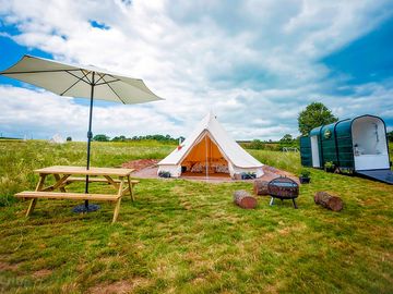 Picnic table, barbecue and bathroom trailer outside the tent