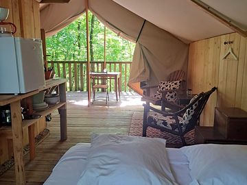 Intérieur tente forestière, literie confortable, coin cuisine et terrasse
