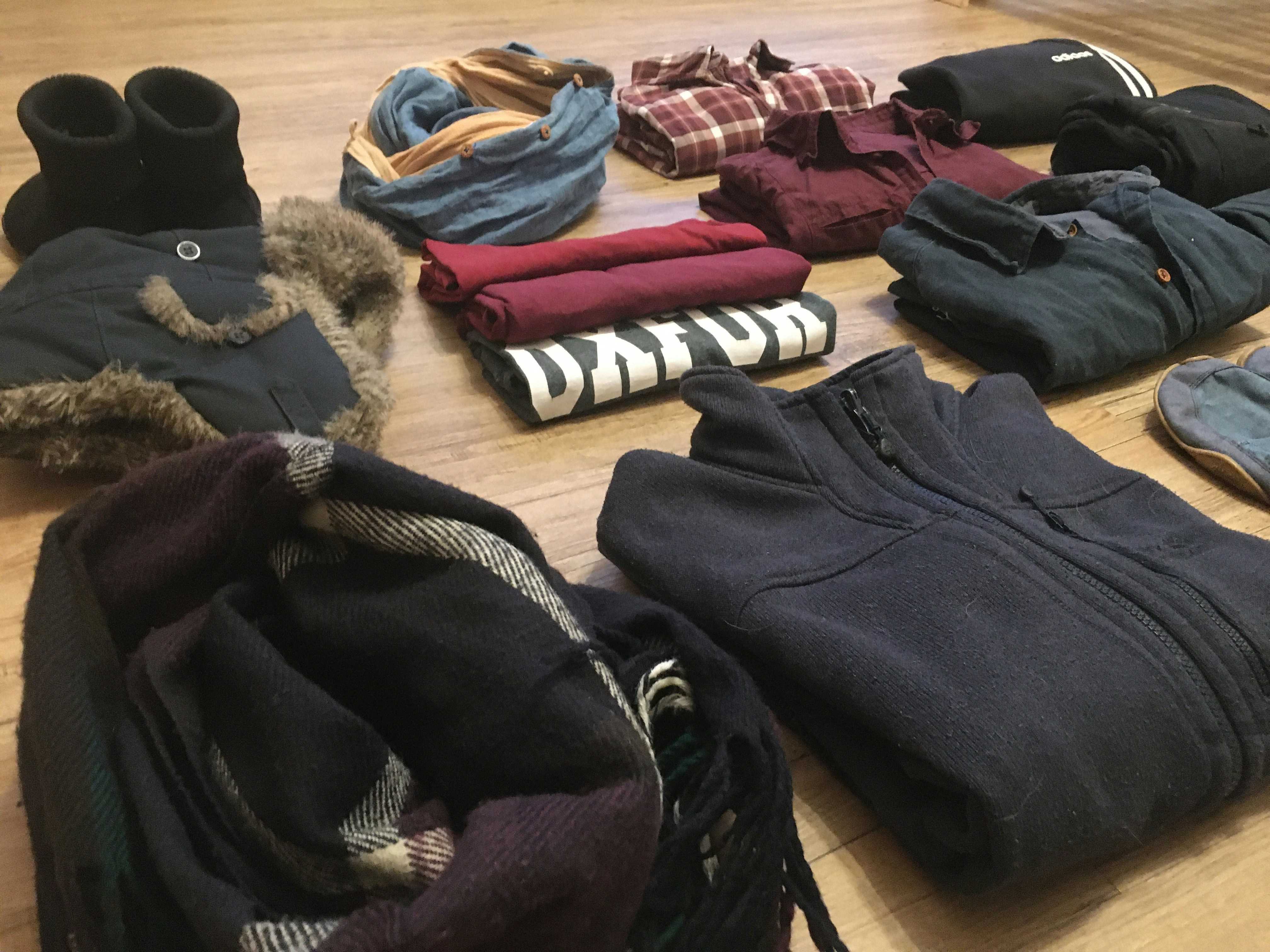 Image shows piles of folded clothes and hats on a wooden floor