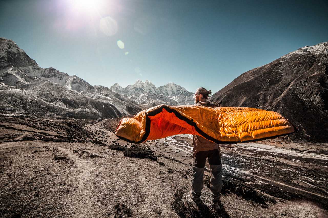 Man holding a sleeping bag in front of a mountain landscape (Martin Jernberg / Unsplash)