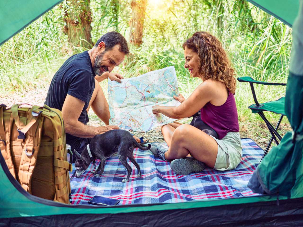 Couple with dog using map to decide which camping activities to participate in (kraken images / Unsplash)