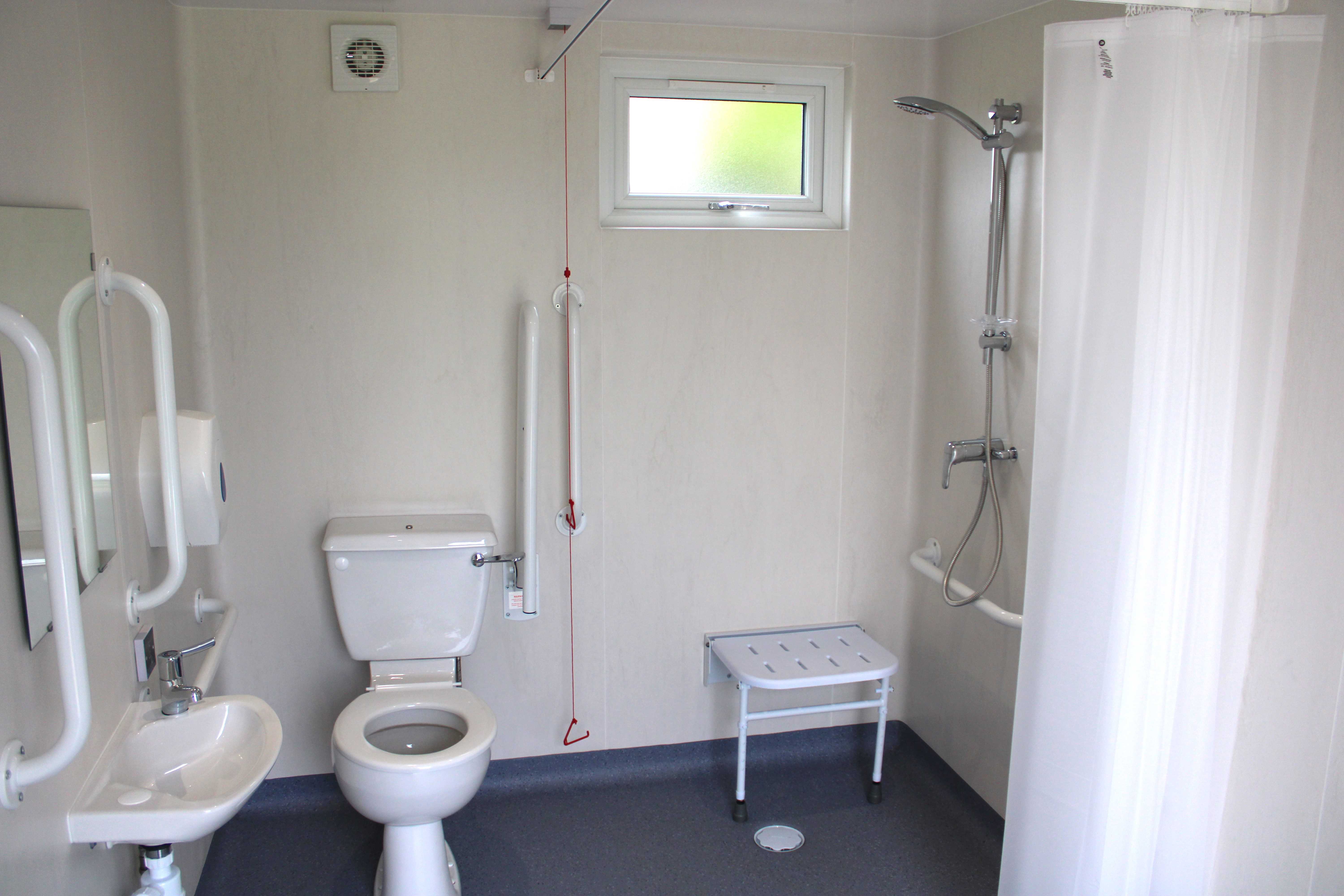 Image of a wheelchair accessible bathroom, with a show and shower chair, and the shower curtain is open