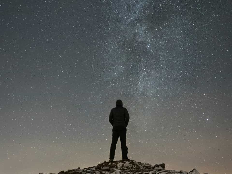 Man standing atop a hill, with the Milky Way in the background