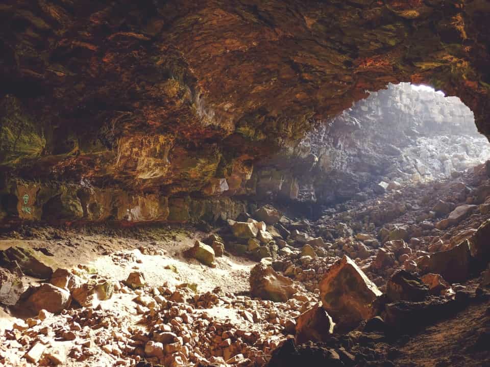 Red cave lit with natural sunlight, many rocks strewn around